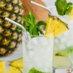 Pinterest graphic for pineapple mojito. Text says "the best pineapple mojito only uses 6 simple ingredients! shakedrinkrepeat.com" Image shows a glass of pineapple mojito with ice, straw, mint leaves, and slice of fresh pineapple. Fresh pineapple surrounding.