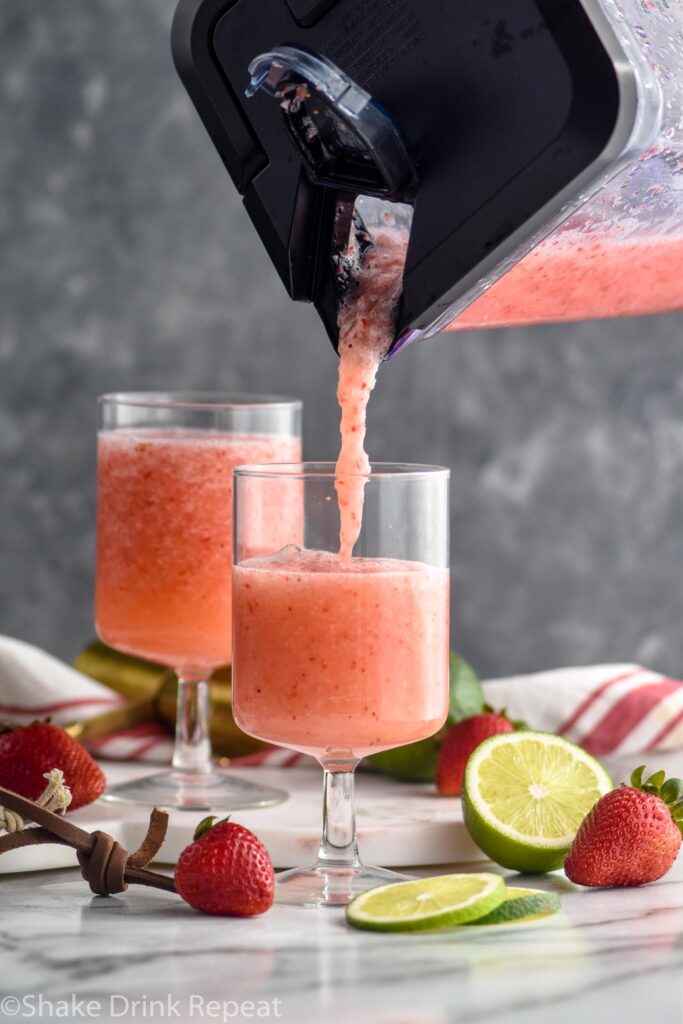 blender of virgin strawberry daiquiri poured into a cocktail glass surrounded by fresh strawberries and limes