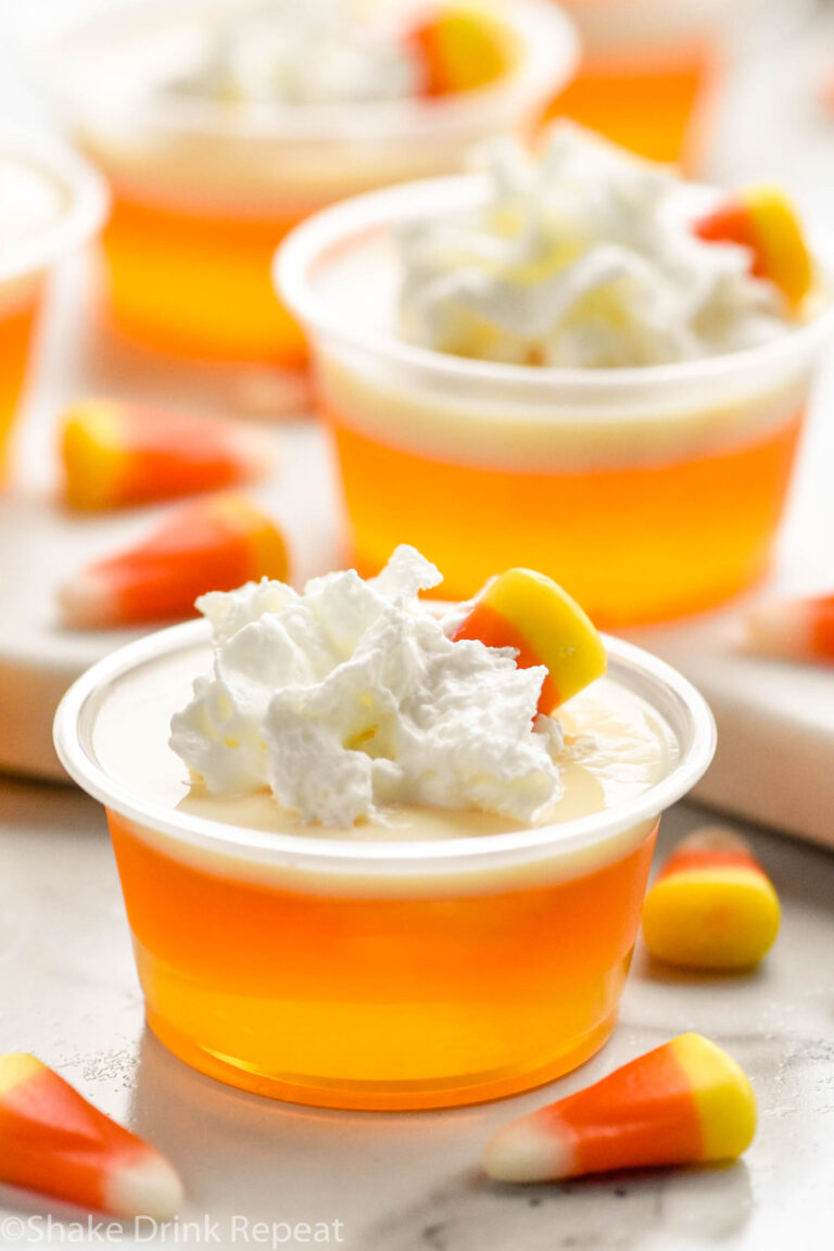 shot glasses of candy corn jello shots topped with whipped cream and candy corn candy