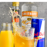 pinterest graphic for cactus cooler shot. Text says "The best cactus cooler shot shakedrinkrepeat.com" Image shows a shot glass splashing into a glass of cactus cooler shot ingredients with with jar of orange juice, can of red bull, bottle of peach schnapps, and bottle of vodka sitting in background.