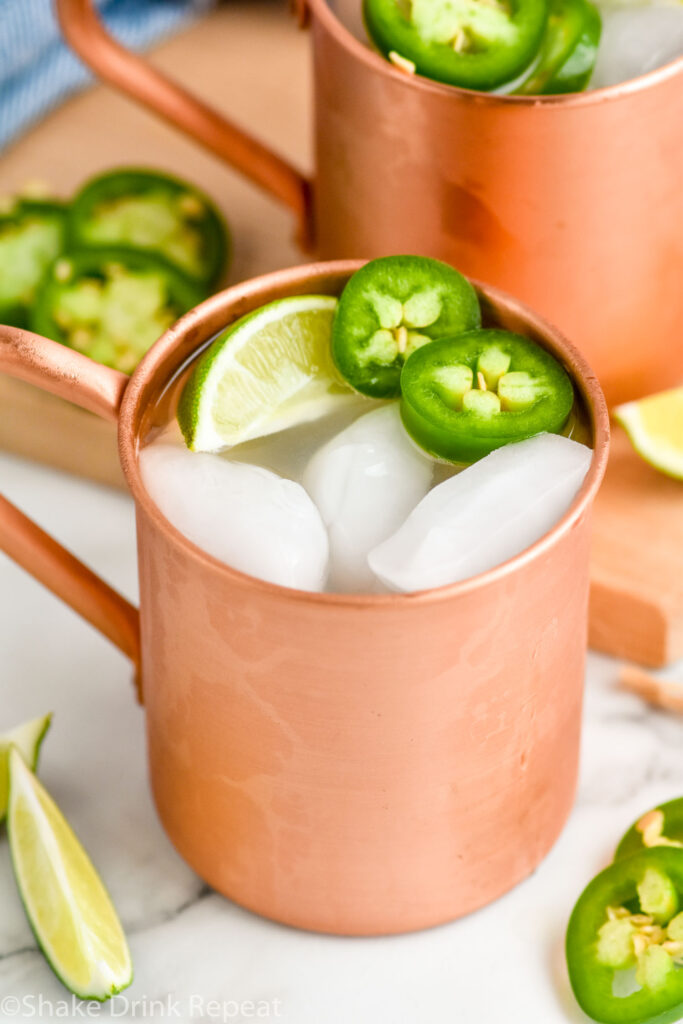 Jalapeno Moscow Mule served in a copper mug with ice. Lime wedge and sliced jalapeno as garnish.