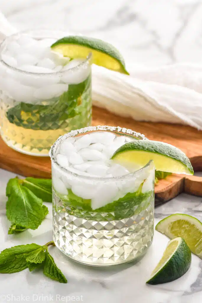 two glasses of Mojito Margarita with fresh mint leaves and lime wedges surrounding