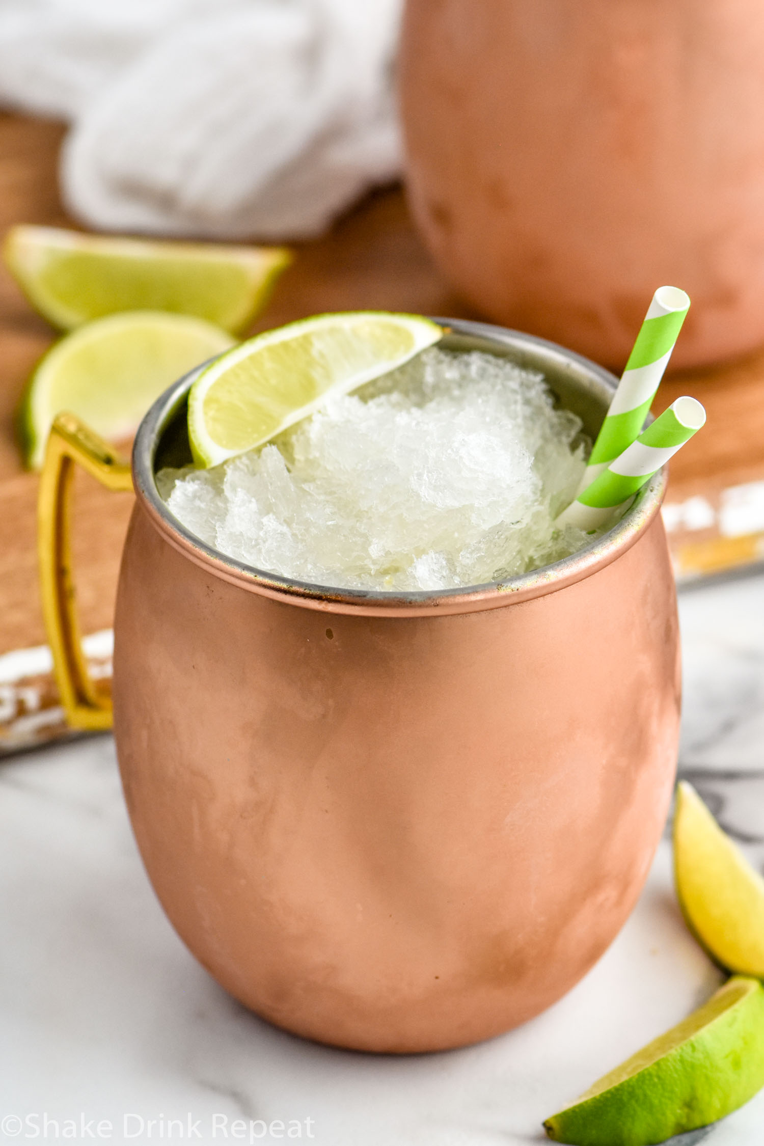 Moscow Mule Slush served in copper mug with straws and lime wedge. Additional lime wedges beside.