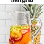 Pinterest graphic for Tropical Margarita Sangria. Text says "the best Tropical Margarita Sangria shakedrinkrepeat.com" Image shows a pitcher of Tropical Margarita Sangria with fresh fruit. Pineapple sitting behind, fresh kiwi and strawberries sitting beside.