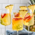 Pinterest graphic for Tropical Margarita Sangria. Text says "the best Tropical Margarita Sangria only uses 10 ingredients! shakedrinkrepeat.com" Image shows 3 wine glasses of Tropical Margarita Sangria with fresh fruit and garnished with a slice of fresh pineapple